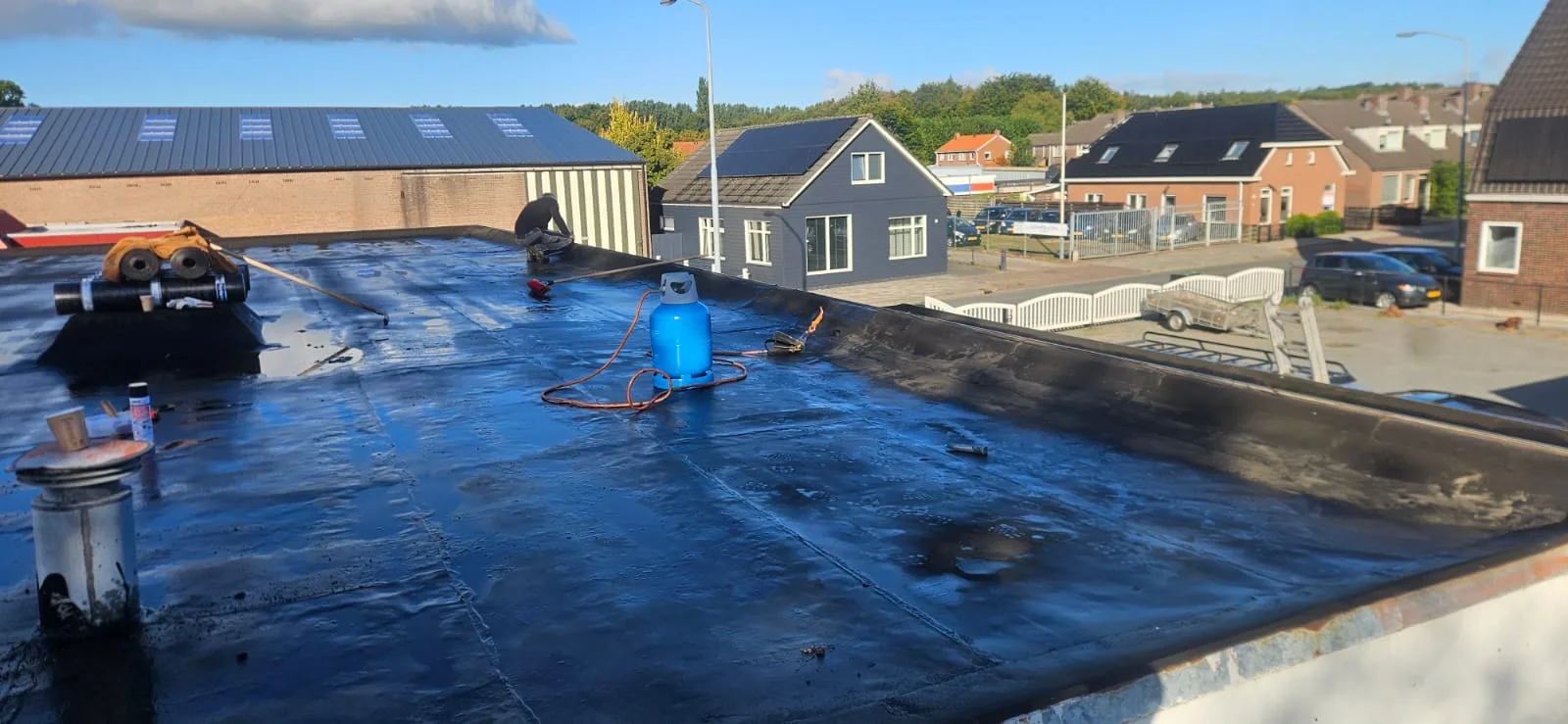 Chantier en cours sur un grand toit plat résidentiel : membrane bitumineuse fraîchement soudée (surface noire brillante).
