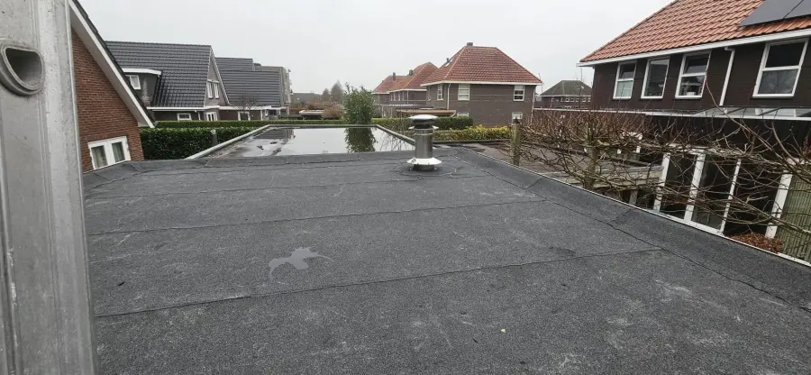 Toiture-terrasse (toit plat accessible) au-dessus d'une extension arrière, photographiée depuis l'étage : surface bitumée plane bordée d'un acrotère maçonné à gauche.