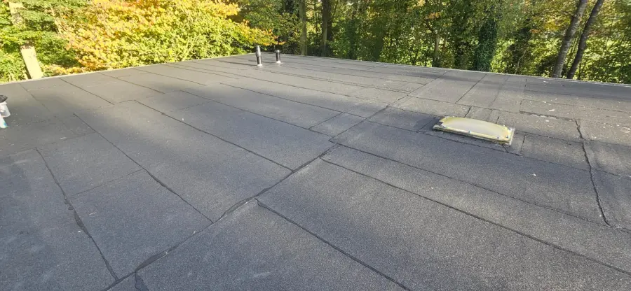 Toit plat résidentiel terminé, vue rasante sur toute la surface : lés de bitume gravillonné soudés, jointures visibles.