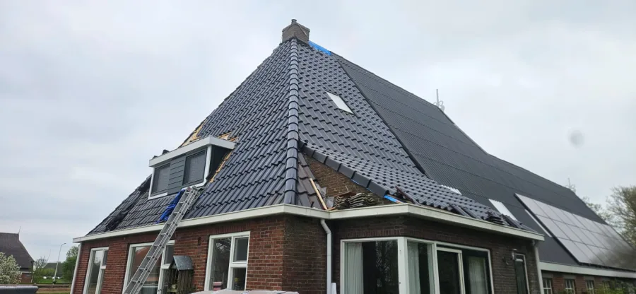 Rénovation d'une toiture en pente : grande toiture à quatre pans d'une maison individuelle en briques rouges.
